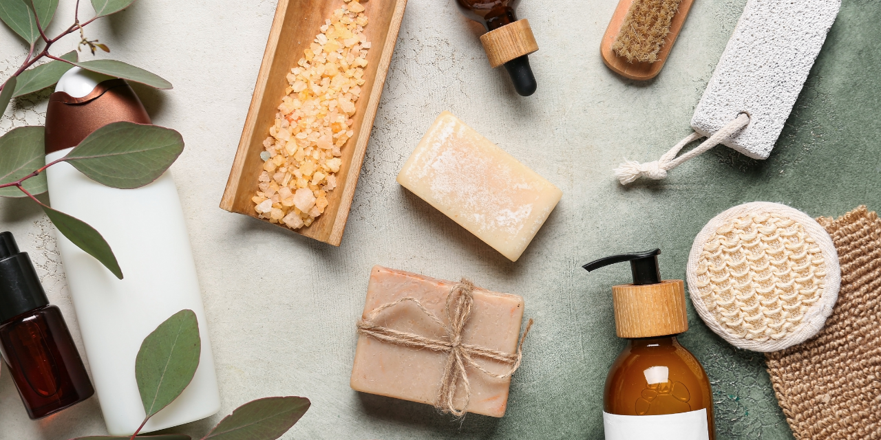 Spa items like soap, lotion, bath salts, and exfoliating tools arranged on a textured surface.